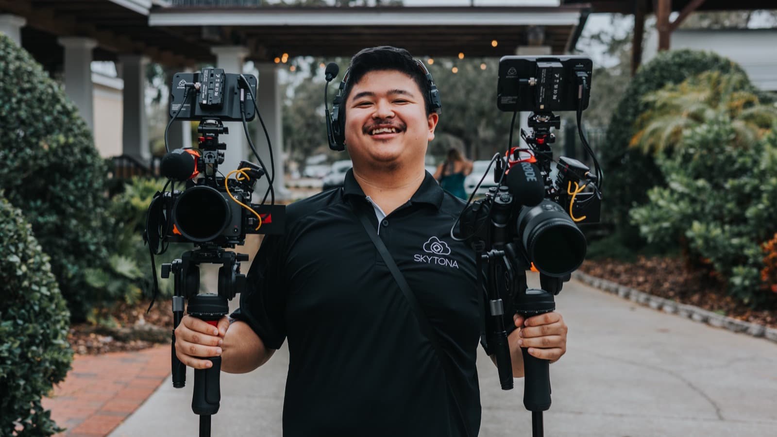 A Skytona filmmaker holding two full camera rigs at a venue entrance.