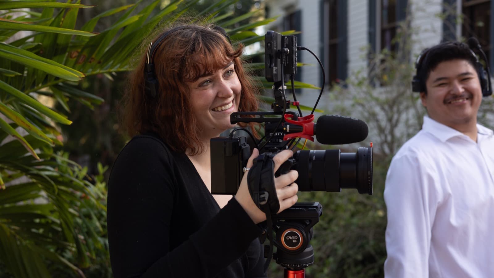 A smiling Skytona filmmaker holding a rigged cinema camera outdoors.